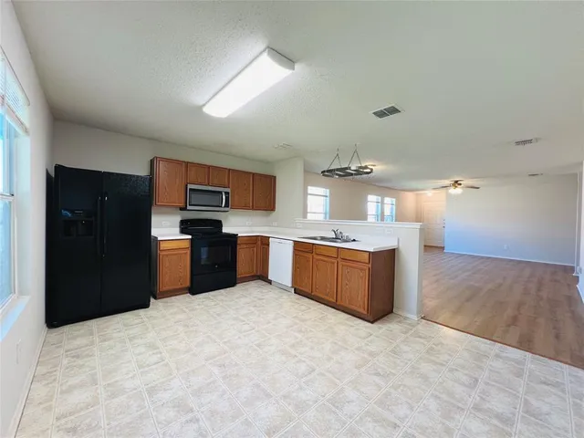 a large kitchen with stainless steel appliances kitchen island a sink dishwasher a refrigerator and black cabinets with wooden floor