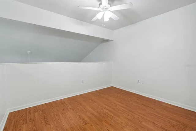 an empty room with a chandelier fan and wooden floor