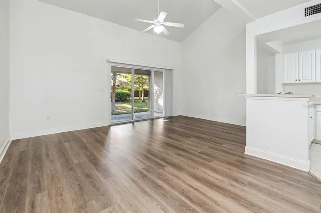 an empty room with wooden floor chandelier fan and windows