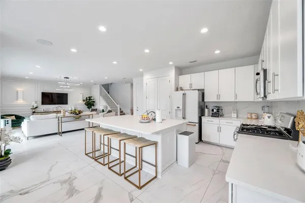 a kitchen with stainless steel appliances kitchen island granite countertop a sink a stove a refrigerator and white cabinets with wooden floor