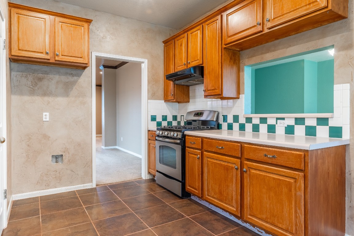 1706 Apache Trail Round Rock, TX 78665 - Photo 13 of 40 Kitchen with stainless steel gas stove, decorative backsplash, light countertops, brown cabinets, and under cabinet range hood