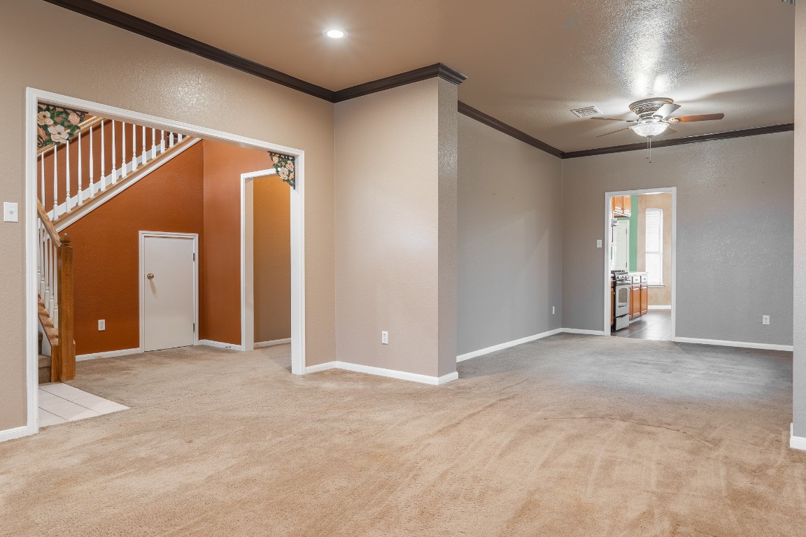 1706 Apache Trail Round Rock, TX 78665 - Photo 7 of 40 Unfurnished living room featuring ornamental molding, a ceiling fan, light colored carpet, stairs, and a textured wall