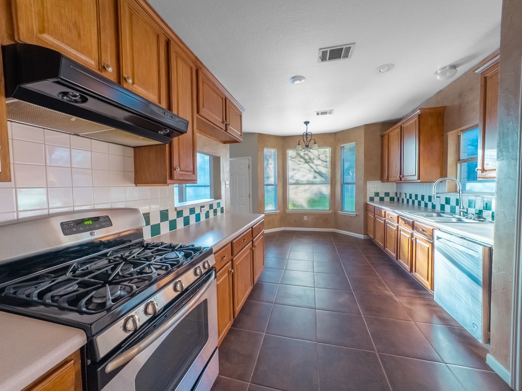 1706 Apache Trail Round Rock, TX 78665 - Photo 9 of 40 Kitchen with appliances with stainless steel finishes, backsplash, under cabinet range hood, brown cabinets, and dark tile patterned floors
