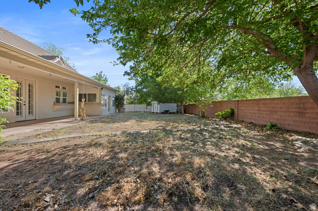 20 Valley Road Leeds, UT 84746 - Photo 33 of 57 Spacious backyard featuring a covered patio, double French doors, mature shade trees, a red brick perimeter wall, and a storage shed