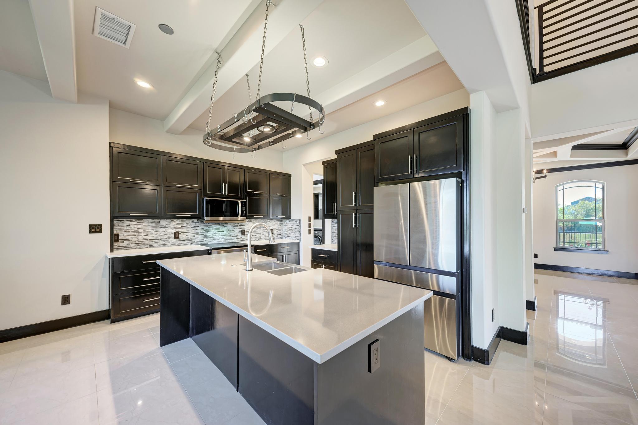 104 Spring Valley Street Hutto, TX 78634 - Photo 14 of 40 Kitchen with beamed ceiling, appliances with stainless steel finishes, light stone countertops, an island with sink, and backsplash