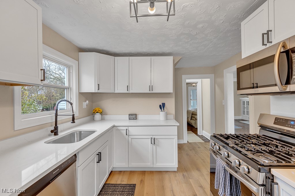 2127 Rossmoor Road Cleveland Heights, OH 44118 - Photo 20 of 21 Kitchen featuring white cabinetry, a sink, light wood-style floors, and appliances with stainless steel finishes