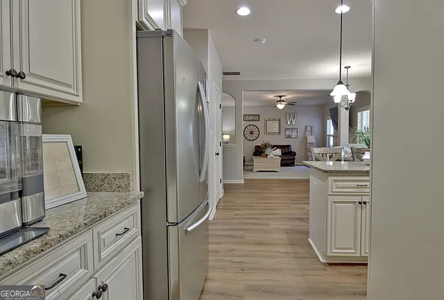 a kitchen with stainless steel appliances kitchen island granite countertop a refrigerator a stove a sink and white cabinets with wooden floor