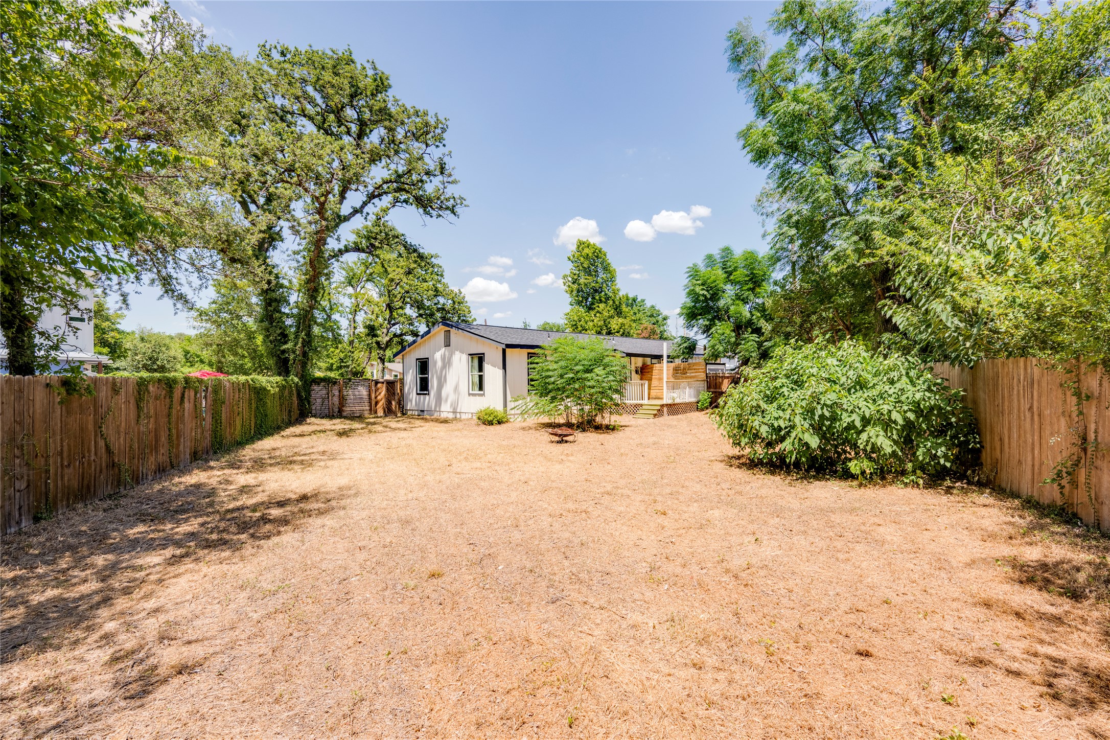 1400 Marcus Place, Unit B Austin, TX 78721 - Photo 35 of 39 A spacious backyard with mature trees, a wooden privacy fence, and a quaint white house.