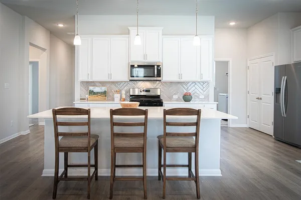 a kitchen with stainless steel appliances granite countertop a dining table chairs refrigerator and microwave