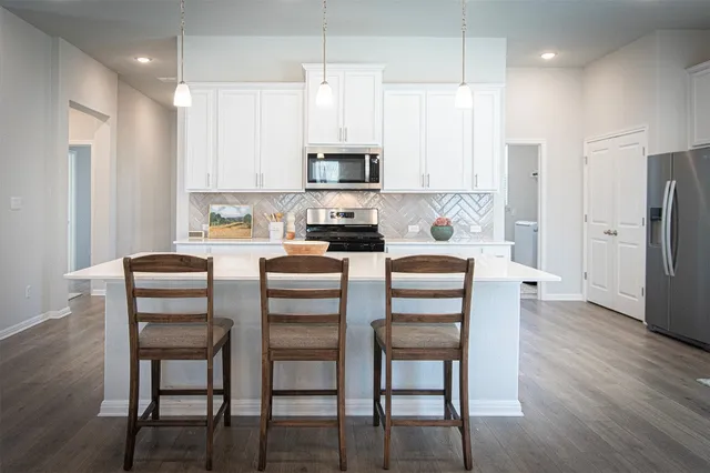 a kitchen with stainless steel appliances granite countertop a dining table chairs refrigerator and microwave