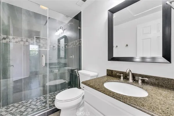 a bathroom with a granite countertop sink a toilet a mirror and shower