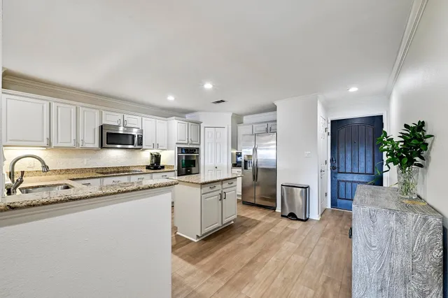 a large kitchen with stainless steel appliances granite countertop a refrigerator a sink dishwasher a stove and white cabinets with wooden floor