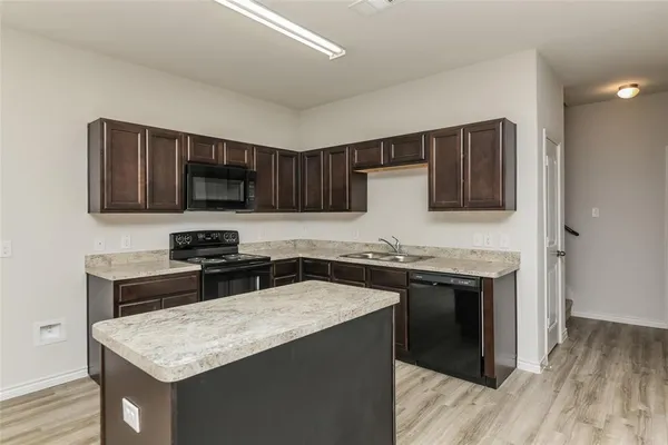 a kitchen with stainless steel appliances granite countertop a stove top oven a sink dishwasher and a refrigerator with wooden floor