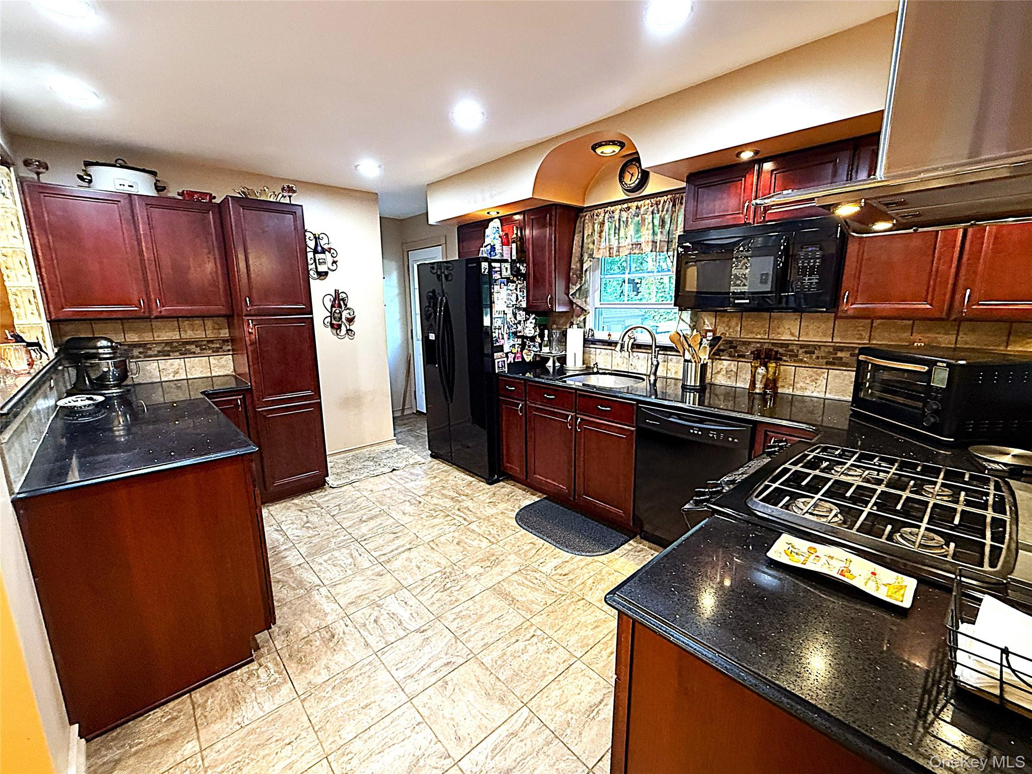 1 Heston Road Shirley, NY 11967 - Photo 11 of 32 Kitchen featuring rich wood cabinetry, black countertops, and a tiled backsplash