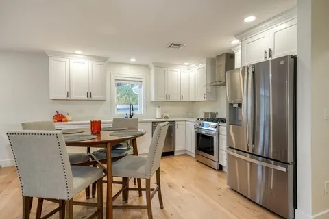 a kitchen with stainless steel appliances a refrigerator a stove a sink and white cabinets with wooden floor
