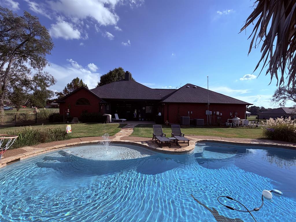 313 An County Road, Unit 2145 Palestine, TX 75801 - Photo 18 of 40 Red-sided exterior with a dark shingled roof, featuring a kidney-shaped swimming pool with a water feature, and a stone-paver pathway