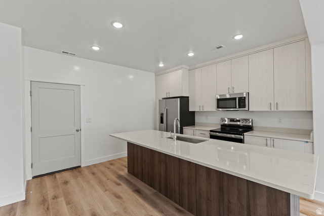 3410 South 1010th Street West Logan, UT 84321 - Photo 3 of 15 Kitchen with appliances with stainless steel finishes, an island with sink, light stone counters, light wood-style floors, and recessed lighting