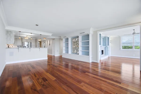 a view of an empty room with wooden floor and a kitchen