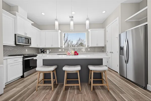 a kitchen with granite countertop a sink stove a refrigerator and white cabinets with wooden floor