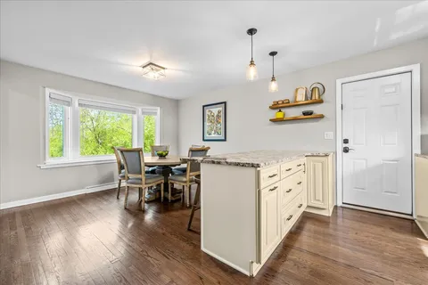 a kitchen with granite countertop a refrigerator a stove a dining table and chairs with wooden floor