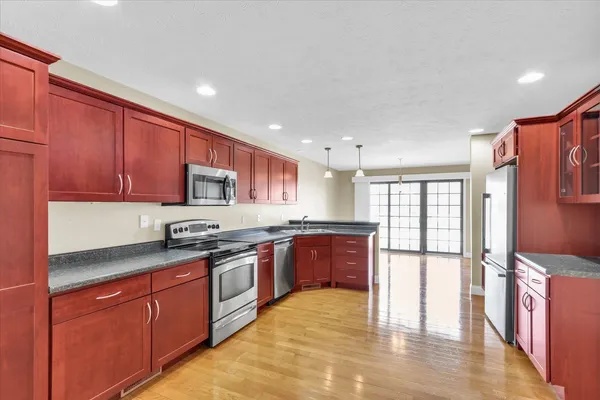 a kitchen with stainless steel appliances granite countertop a refrigerator a sink dishwasher a stove top oven and a dining table with wooden floor
