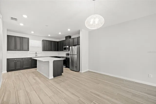 a large kitchen with stainless steel appliances a large counter top a sink and a chandelier