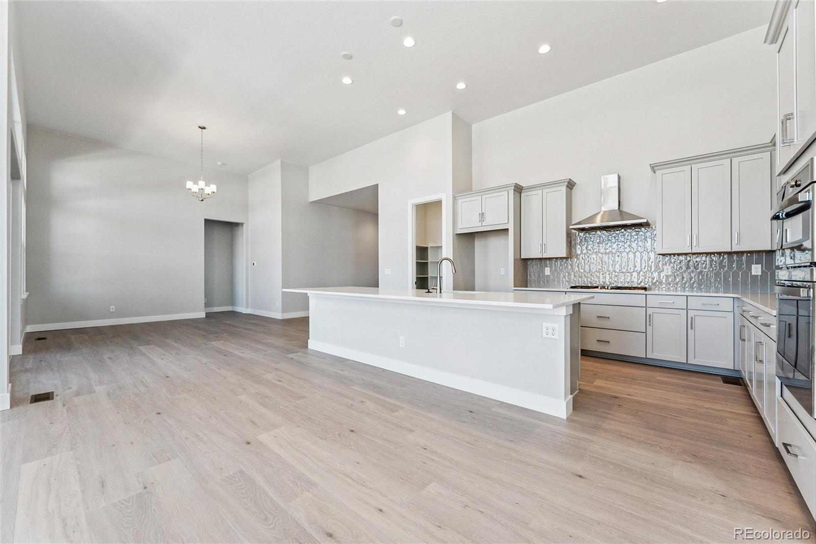 3877 Freestone Point Castle Rock, CO 80108 - Photo 9 of 48 a large white kitchen with kitchen island a sink a stove a refrigerator and white cabinets with wooden floor