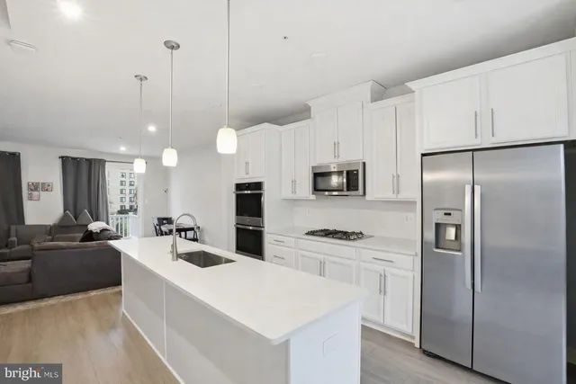 a large kitchen with kitchen island a refrigerator a stove a sink a center island and couches with wooden floor