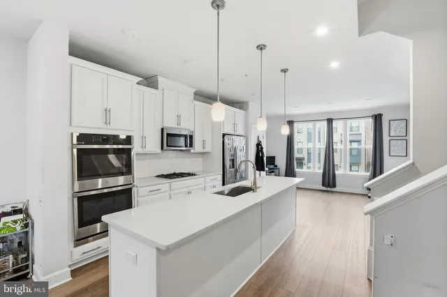 a kitchen with stainless steel appliances kitchen island granite countertop a refrigerator a stove a sink dishwasher and white cabinets with wooden floor