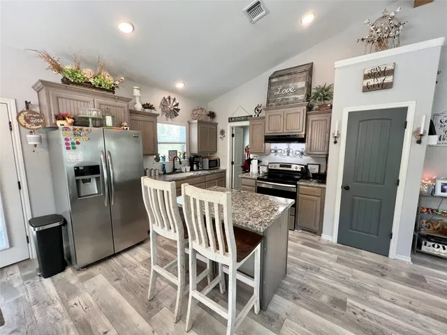 a kitchen with stainless steel appliances granite countertop a refrigerator a stove a microwave oven a sink with island and chairs