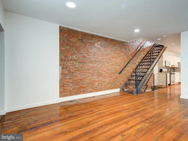 a view of an empty room with wooden floor stairs and a way to kitchen with window
