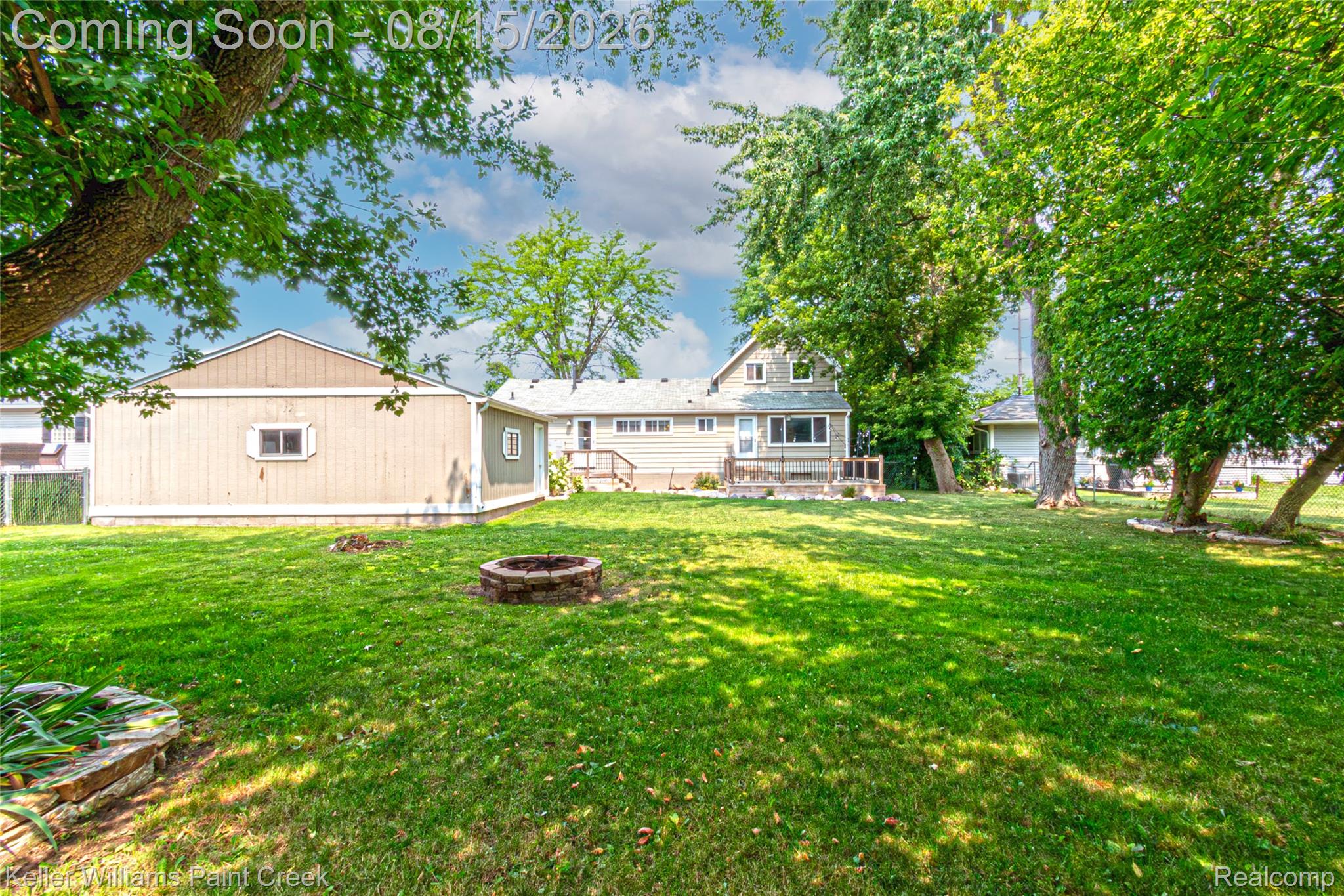 Expansive green lawn with mature shade trees, a stone-ringed fire pit, and a detached structure with siding