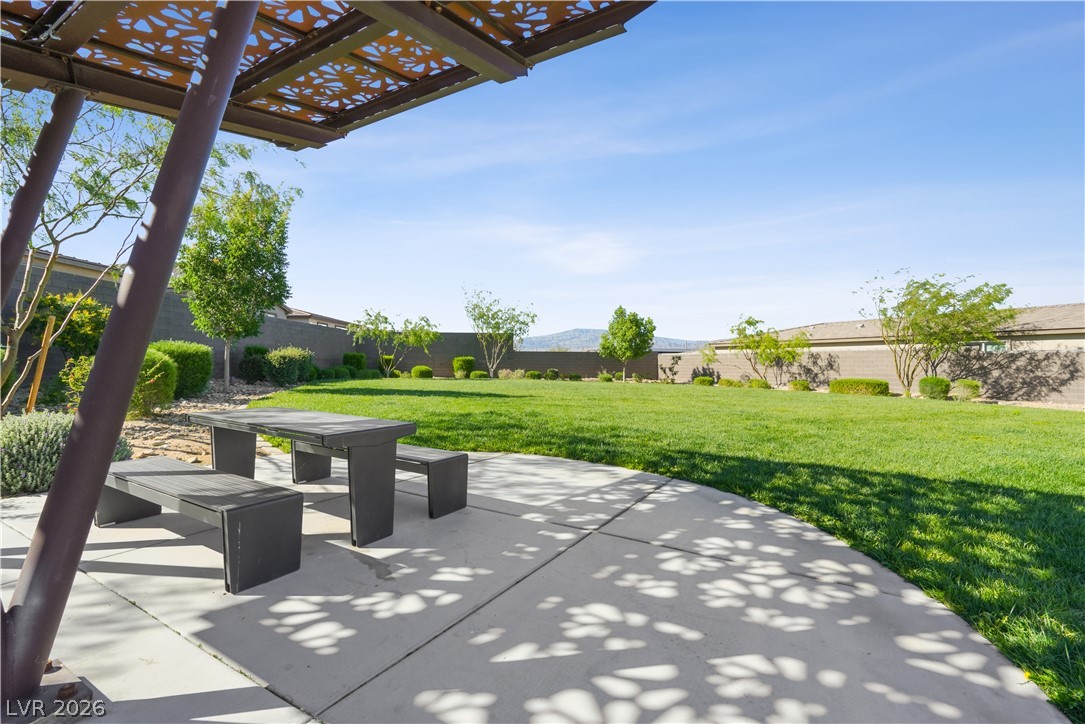 9398 Noble Fir Rdg Court Las Vegas, NV 89143 - Photo 34 of 36 An inviting outdoor patio with a shaded dining area overlooks a well-maintained, verdant yard.