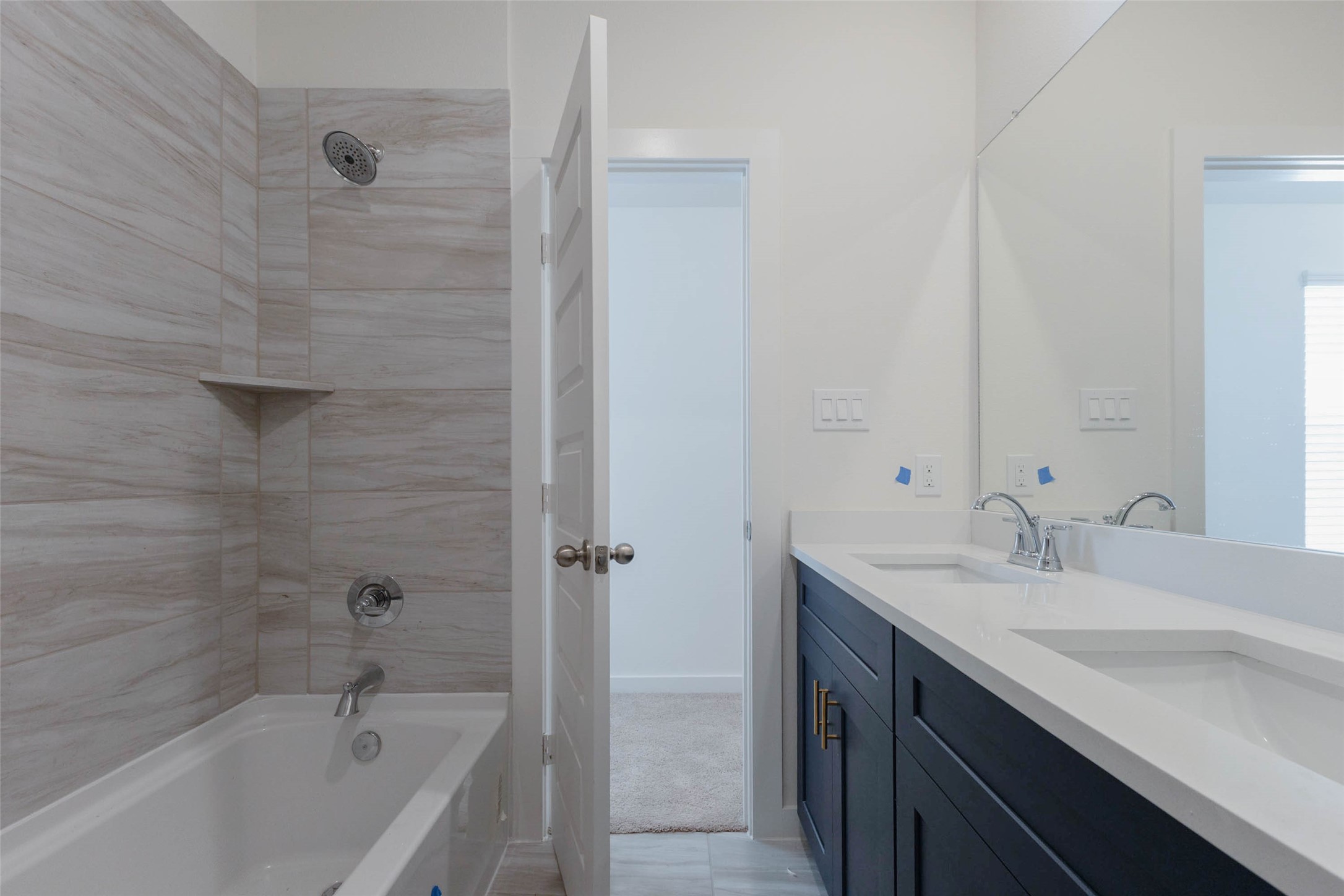 1115 Santee Court Rosharon, TX 77583 - Photo 18 of 23 A closer look at the shared bath shows a tub-shower wrapped in wood-grain tile with a built-in corner shelf for toiletries. Next to it, the double-sink vanity offers lots of drawer and cabinet space, and a doorway leads straight to the hall for easy access from the bedrooms. It is a clean, stylish bathroom designed to handle busy mornings.