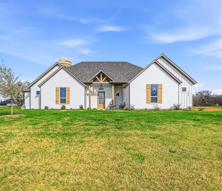 1005 Ronnie Court Springtown, TX 76082 - Photo 4 of 27 White brick exterior featuring dark shingle roofing and natural wood shutters