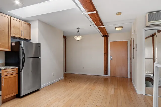 a view of a refrigerator in kitchen and an empty room with wooden floor and windows