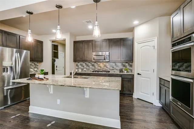 a kitchen with stainless steel appliances granite countertop a sink a stove a refrigerator and a oven with wooden floor