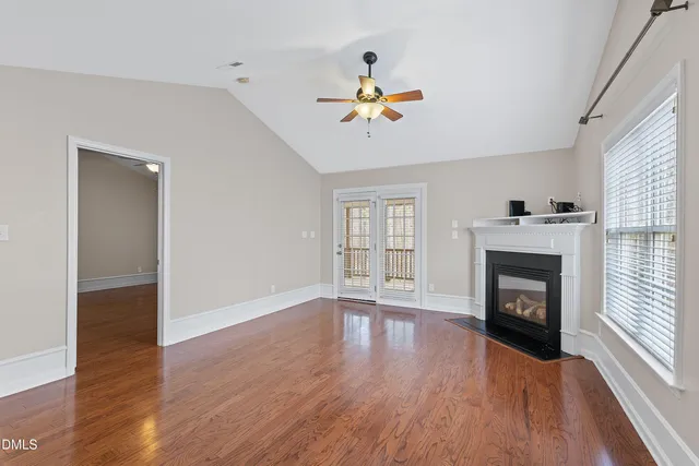 an empty room with wooden floor fireplace and windows