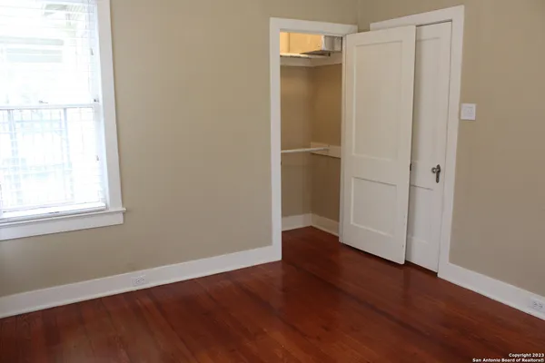 an empty room with wooden floor closet and windows