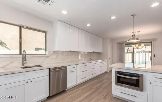 a kitchen with stainless steel appliances granite countertop a stove a sink and white cabinets with wooden floors