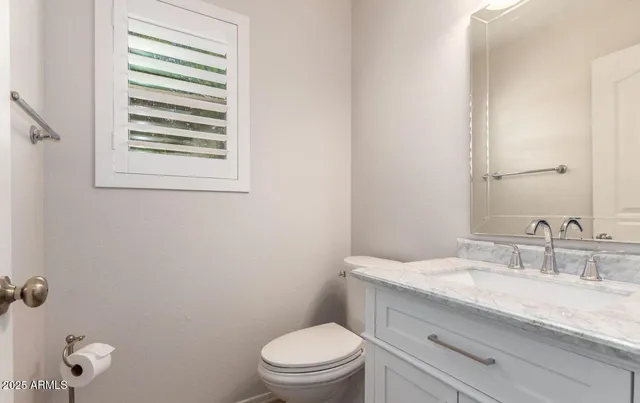 a bathroom with a granite countertop toilet a sink a mirror and a window
