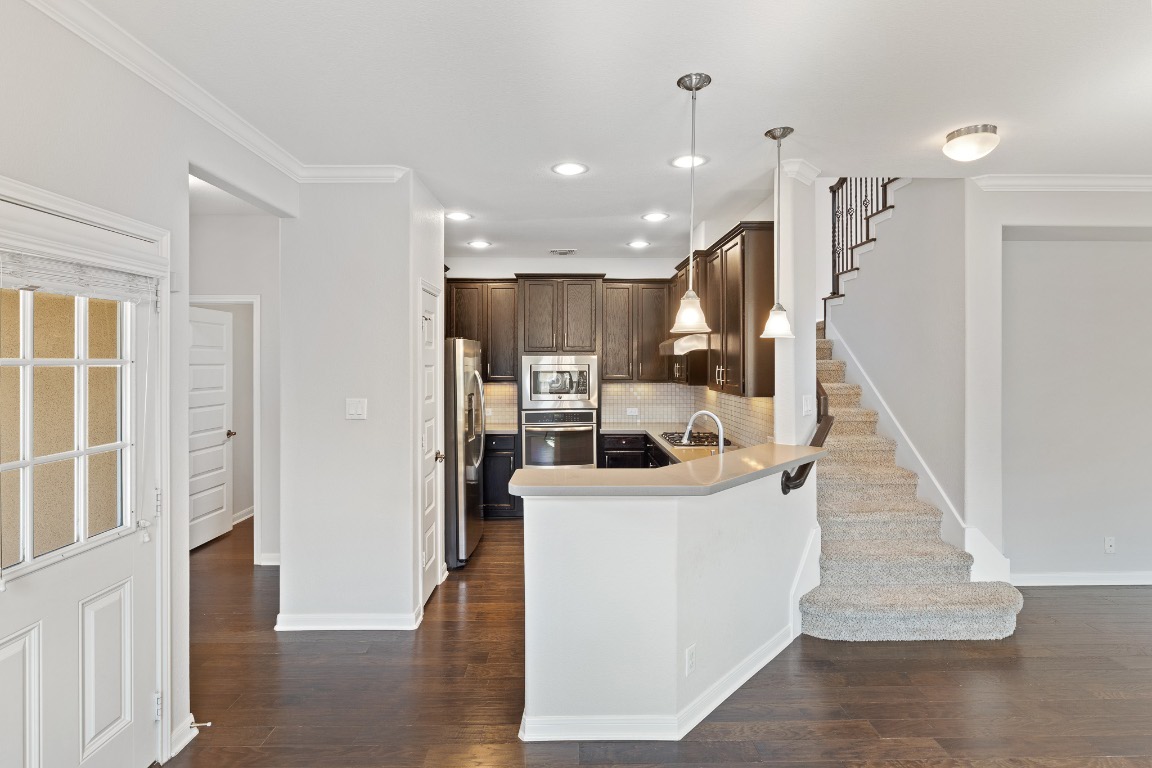 506 Hummingbird Lane, Unit A Austin, TX 78734 - Photo 4 of 36 Kitchen with dark brown cabinetry, decorative backsplash, stainless steel appliances, decorative light fixtures, and ornamental molding