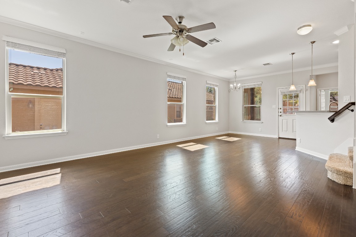 506 Hummingbird Lane, Unit A Austin, TX 78734 - Photo 6 of 36 Unfurnished living room with crown molding, dark wood-style flooring, a chandelier, a ceiling fan, and stairway