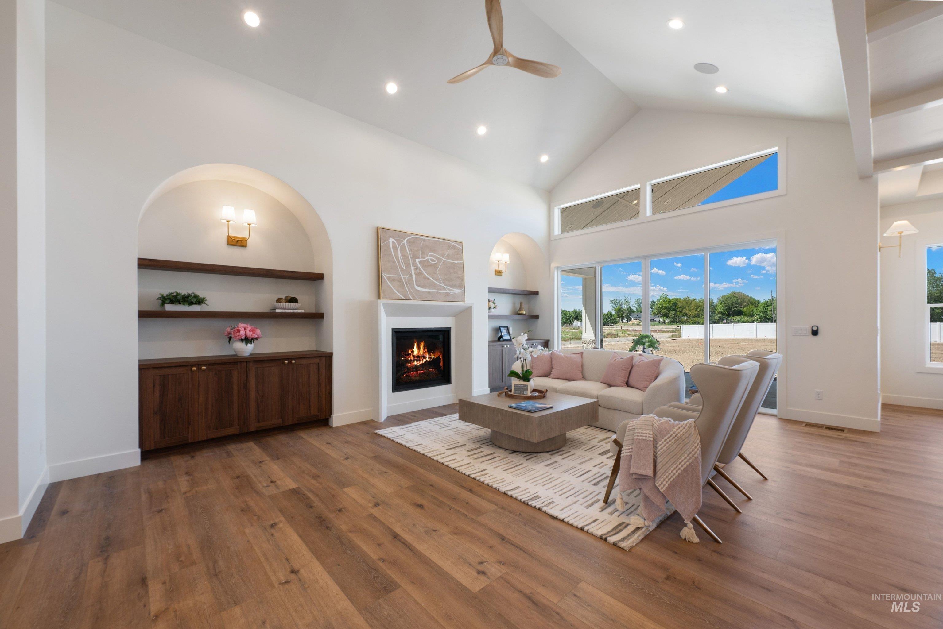 24821 Ardmore Court Caldwell, ID 83607 - Photo 11 of 43 Vaulted ceiling living space featuring a fireplace with white mantel, wood-finish flooring, built-in cabinetry with open shelving, and large windows with transom lighting