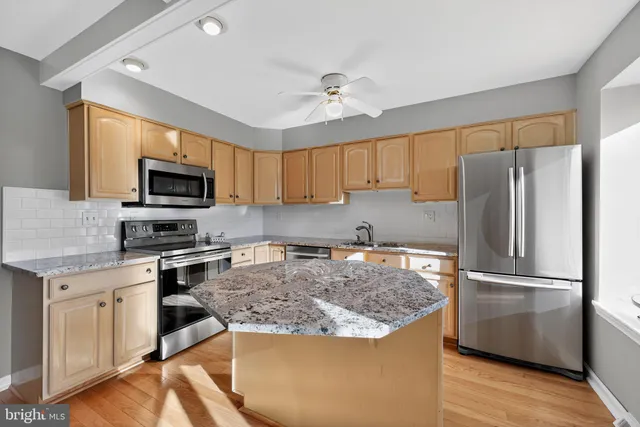 a kitchen with granite countertop a refrigerator a sink a stove a microwave and wooden cabinets