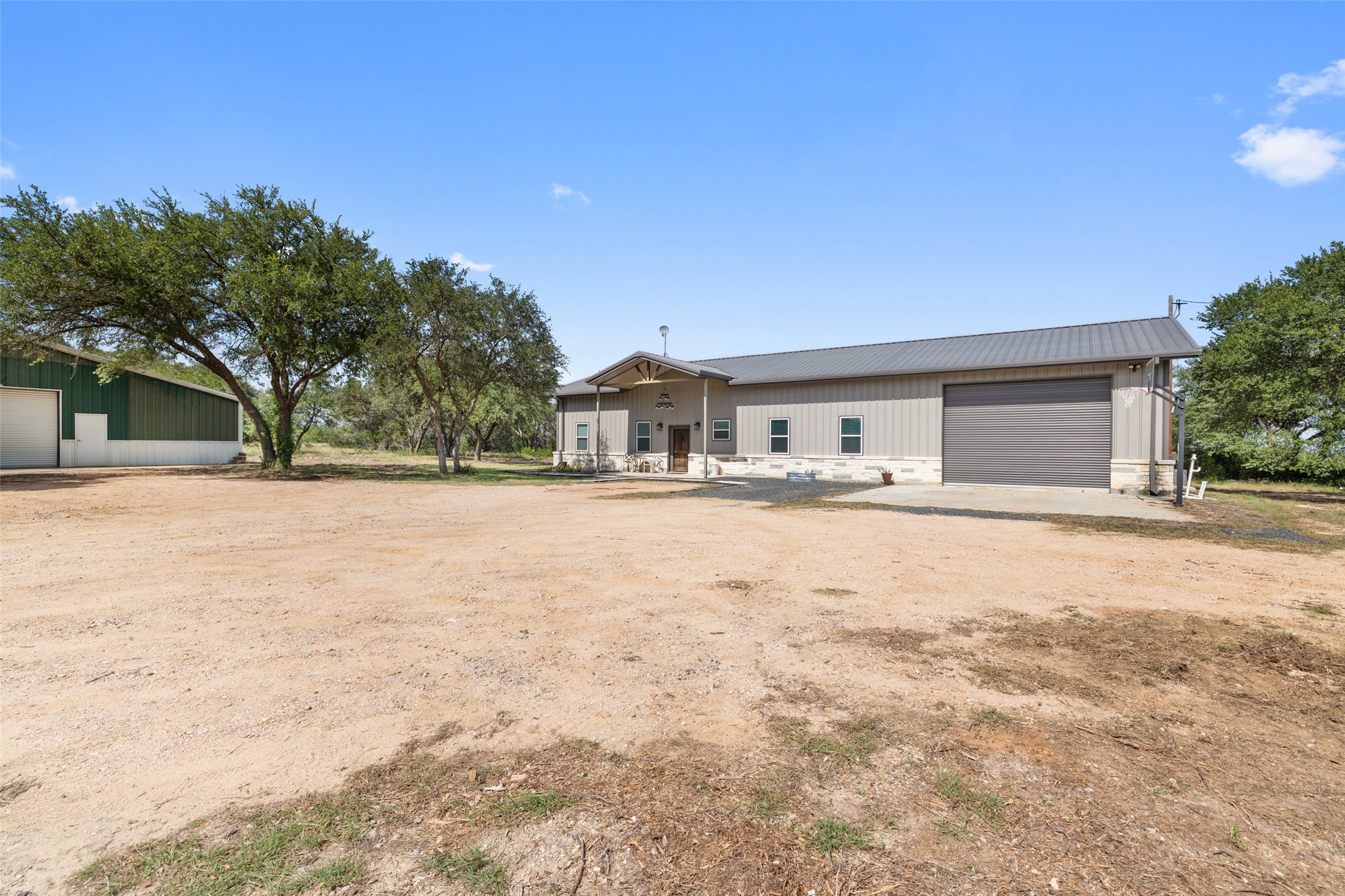 A spacious barndominium features a front entry porch and an attached garage door, set against a clear blue sky.