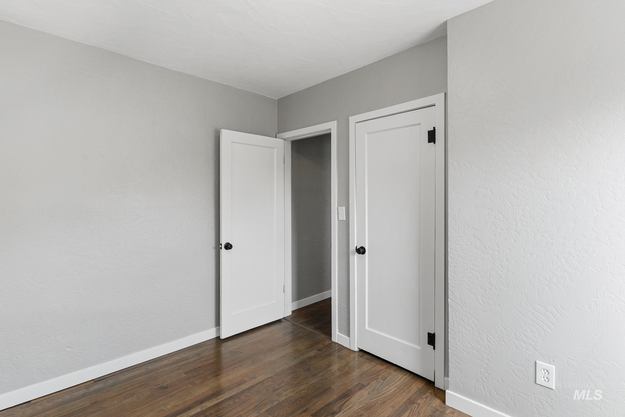 619 Thain Road Lewiston, ID 83501 - Photo 24 of 44 Interior room featuring wood-finish flooring, light grey painted walls, white baseboards, and two white panel doors with black hardware