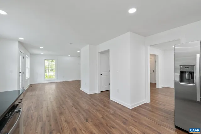 a view of empty room with wooden floor and kitchen