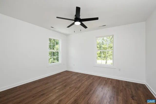 an empty room with wooden floor ceiling fan and windows