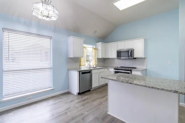 a kitchen with stainless steel appliances granite countertop a sink a stove a microwave a refrigerator a window and white cabinets